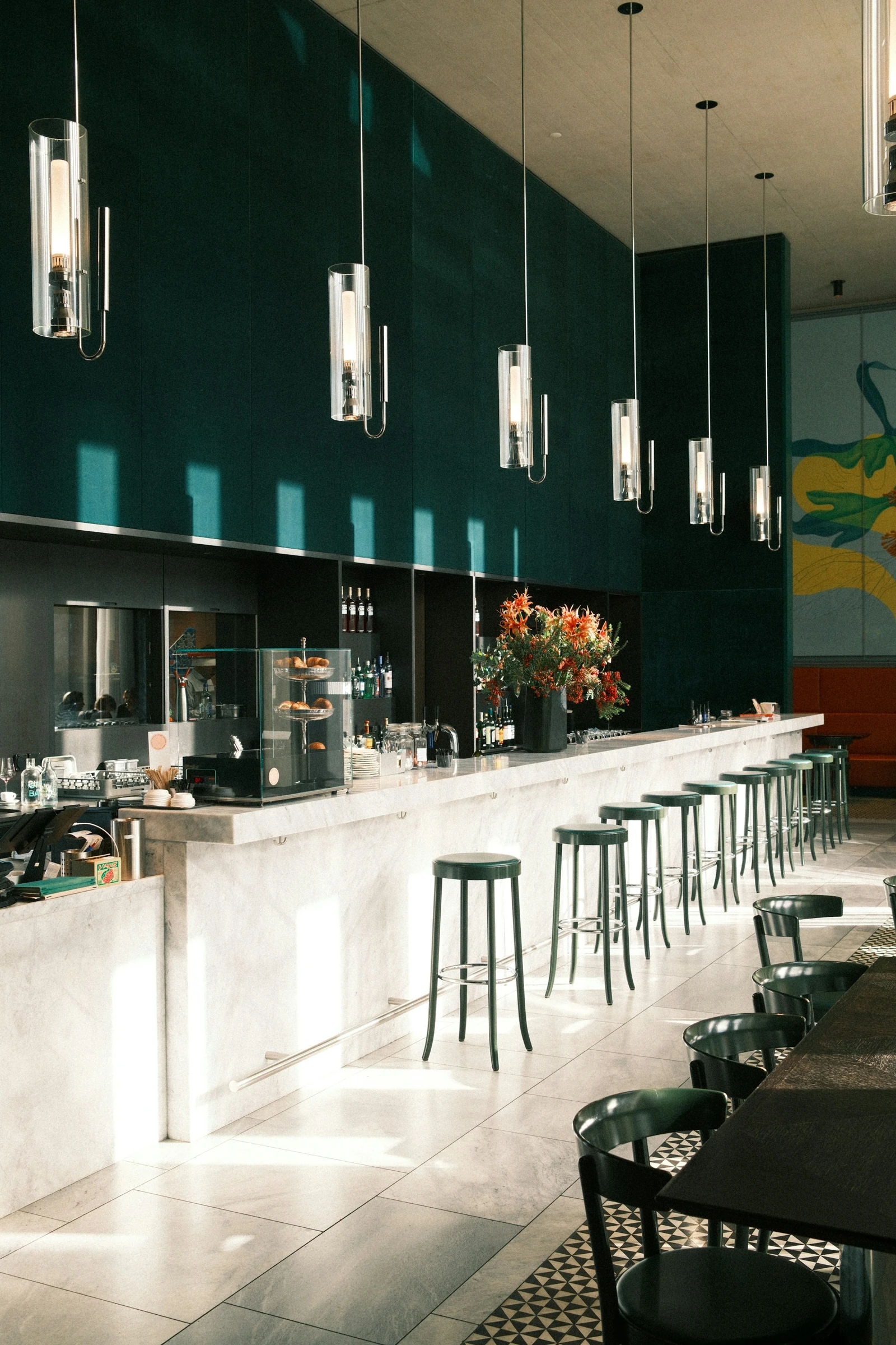 Contemporary restaurant bar with a pale marble counter, green seating and architectural pendant lighting